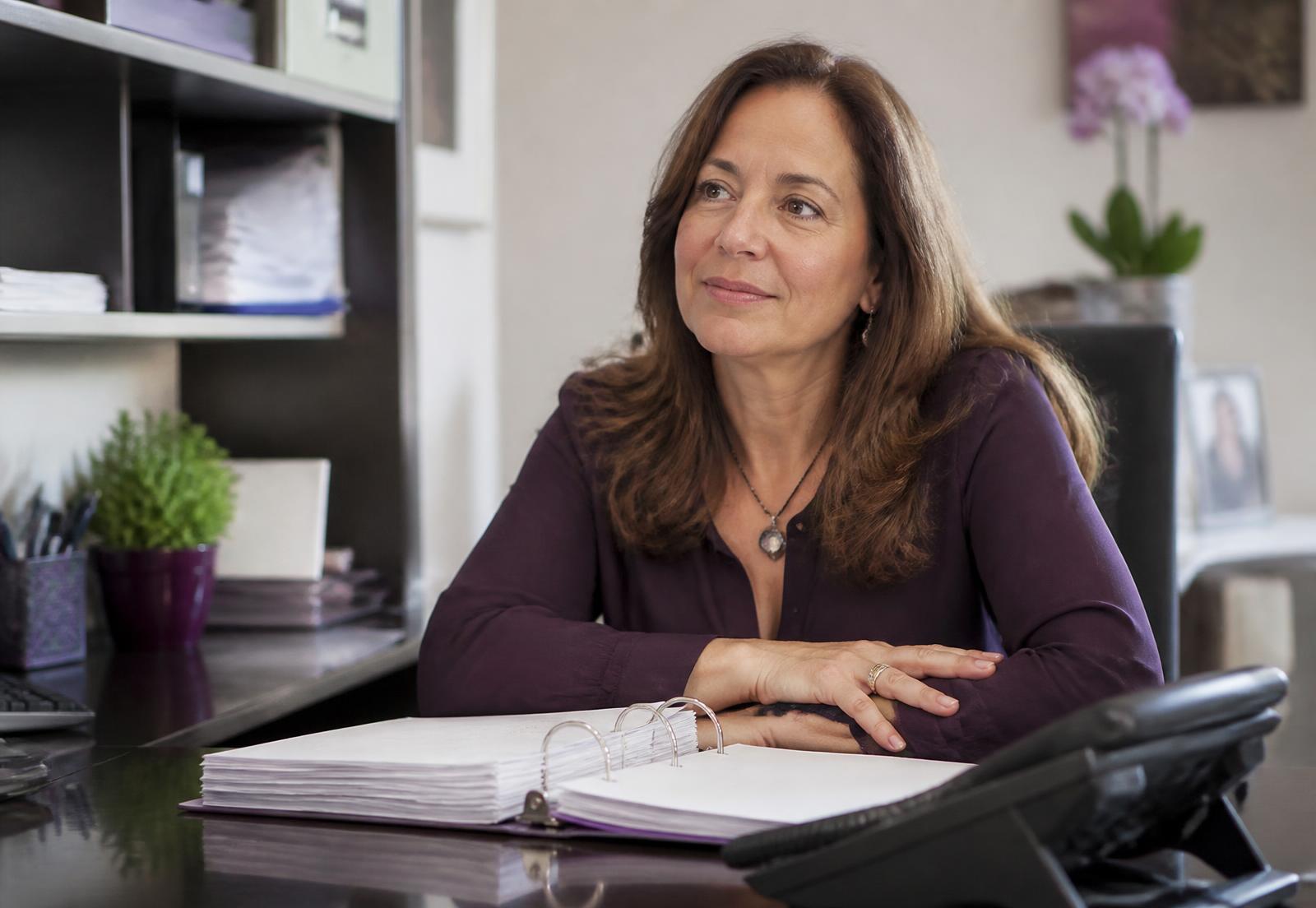 Clinic office manager at her desk with the practice protocol binder open beside the phone